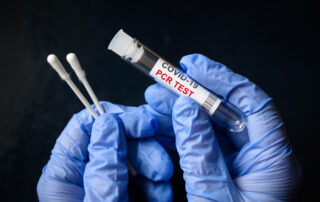 A lab worker is holding two swabs and a container for a COVID-19 PCR test in their gloved hands